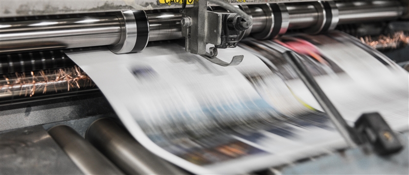 A newspaper mid-print in large industrial printer. Photo by Bank Phrom via Unsplash.